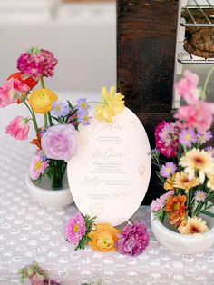 colorful flowers in small vases sitting on a table next to an empty card board