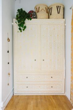 a white cabinet with baskets on top of it next to a wooden floor and yellow curtains