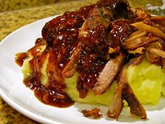 a white plate topped with mashed potatoes covered in bbq sauce and pulled pork