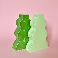 two green vases sitting next to each other on a pink surface