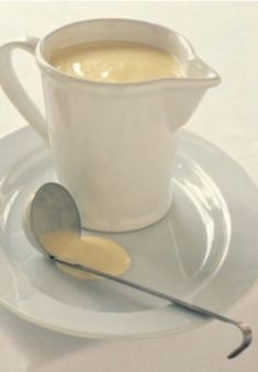 a white plate topped with a cup and saucer next to a spoon on top of it