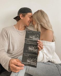 a man and woman sitting next to each other on a couch holding up an album