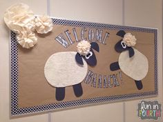 a welcome sign with two sheep and flowers on the front, attached to a wall