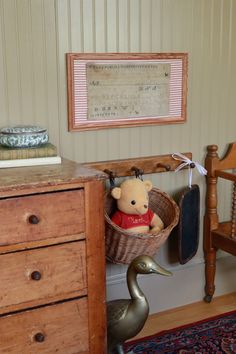 a teddy bear sitting in a basket on top of a dresser next to a bird