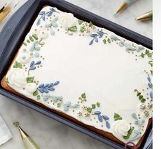 a cake with white frosting and blue flowers on it sitting in a baking pan