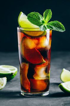 a glass filled with ice, lime and mint on top of a table next to sliced limes