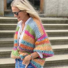 a woman walking down the street wearing a multicolored cardigan sweater and jeans