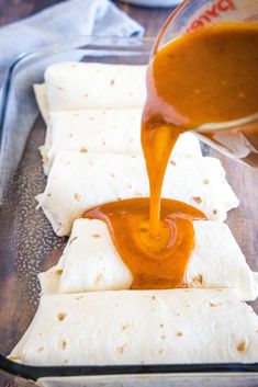 someone pouring sauce onto tortillas on a tray