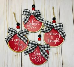 four christmas ornaments hanging on a white wooden background with the words believe, merry and bright