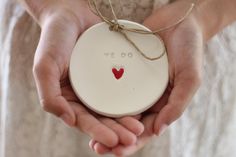 two hands holding a white ceramic ornament with a red heart on the front