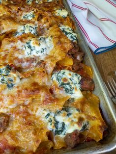 a casserole dish with meat, cheese and spinach on it next to a fork