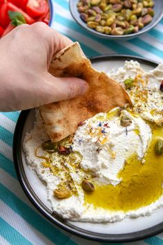 a person is dipping some food into a bowl with olives and pistachio