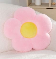 a pink flower shaped pillow sitting on top of a white couch next to a shelf