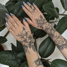 two women's hands with tattoos and flowers on their arms next to green leaves