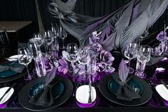 the table is set with black and purple plates, silverware, and napkins