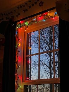 an open window with christmas lights hanging from it's sides and trees in the background