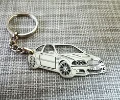 a key chain with a car on it sitting on a gray fabric surface, showing the front end of a white bmw