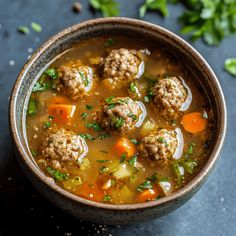 a bowl filled with meatball soup on top of a blue countertop next to parsley