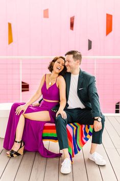 a man and woman sitting on a bench in front of a pink wall with geometric shapes