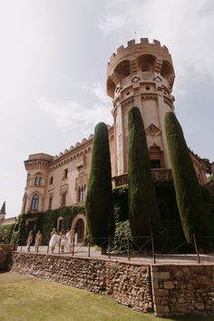 a large castle like building with tall trees on the sides and people walking around it