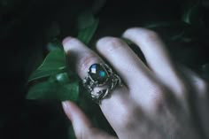 a person's hand holding a ring with a stone in it and leaves around it