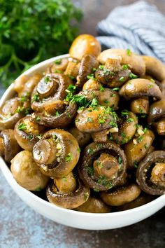 a white bowl filled with mushrooms and parsley on top of a gray countertop