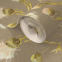 a roll of wallpaper with gold and white flowers on grey background, next to a rolled up piece of paper