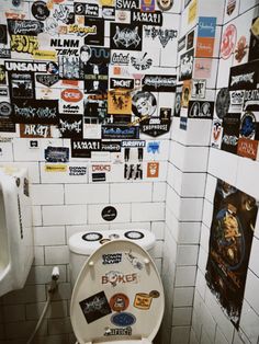 a white toilet sitting in a bathroom next to a wall covered with stickers and decals