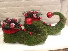 two red and green christmas decorations sitting on top of a white table next to a brick wall