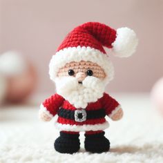 a small crocheted santa clause is standing on a white carpet with his hands in his pockets