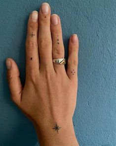 a person's hand with two small tattoos on their fingers and one has a star tattoo on the middle finger