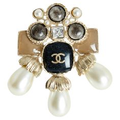 Chanel brooch AW2016 collection in lightly gilded metal (between gold and silver), XL format, central cabochon covered with slightly glittery black enamel and inlaid with a CC logo, cabochons of different shapes and slightly glittery colors, fancy pearls and white rhinestones. Width 5.9 cm x height 6.5 cm. The brooch is delivered without original invoice, in a pretty Chanel box, it is perfect with everything, every day... Broche Chanel, Chanel Ring, Chanel Brooch, Chanel Box, Chanel Accessories, White Rhinestone, Cc Logo, Black Enamel, Gold And Silver