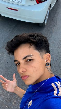 a young man with piercings on his ears standing in front of a white car