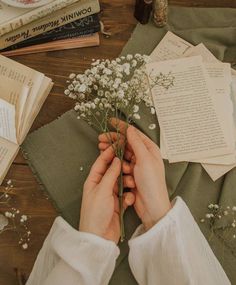 a person holding flowers on top of a wooden table next to books and other items