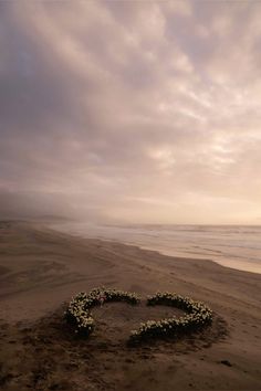 a heart made out of flowers sitting on top of a sandy beach next to the ocean