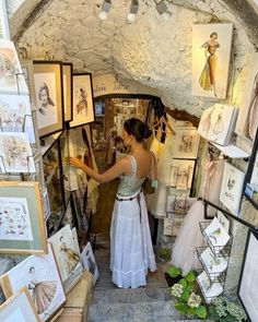 a woman in a white dress is looking at pictures on the wall and holding her hand out