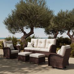 an outdoor seating area with wicker furniture and olive trees in the back ground, overlooking the ocean