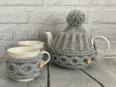 a knitted tea pot and two cups on a wooden table