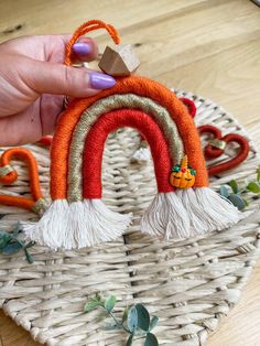 a hand holding a small orange and white rainbow ornament on top of a wicker basket