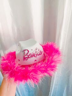 a pink hat with the word barbie on it sitting in front of a white curtain