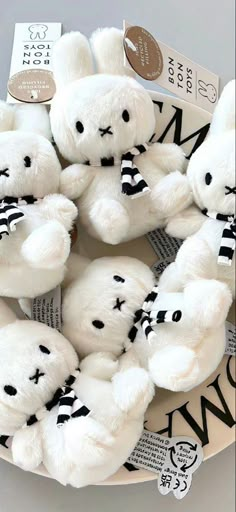 several white teddy bears sitting on top of a plate with black and white tags around them