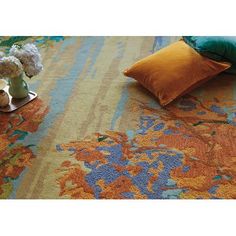 an orange, blue and yellow rug with flowers on the floor next to it in front of a pillow