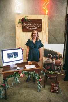 a woman standing in front of a desk with a computer on it and flowers around the desk