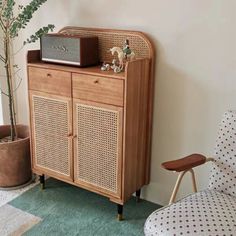 a wooden cabinet sitting next to a chair and potted plant in a living room