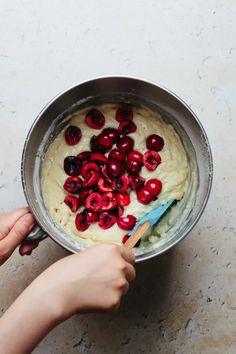 a person holding a spoon in a bowl filled with cream and cherries