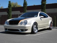 a white car parked in a parking lot next to a tall brown fence and trees