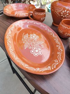 an orange plate with white designs on it sitting on a table next to cups and saucers