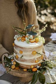 a woman is holding a cake with oranges on it and greenery around the edges