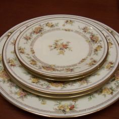 three white and gold plates with flowers on them sitting on a wooden table top next to each other