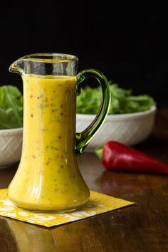 a yellow pitcher sitting on top of a wooden table next to a bowl of lettuce